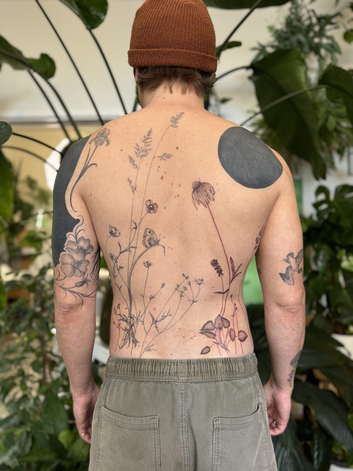 Fine-line wild meadow and wildflower back tattoo flowing up the spine, by Gosia, Bristol